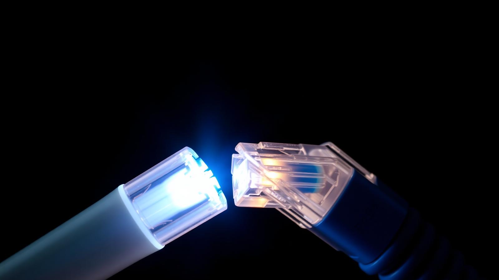Cinematic macro photograph of a fibre optic cable with glowing blue light next to a coiled blue Cat6 ethernet cable